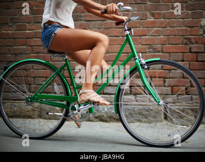 Close-up di giovane donna equitazione Bicicletta contro un muro di mattoni Foto Stock