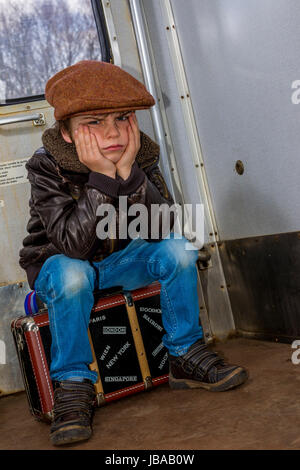 Vintage Ragazzo seduto sulla sua valigia nella hall di un treno Foto Stock