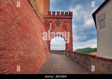 Stretta viuzza acciottolata lungo rosso parete in mattoni e con il frammento del borgo medievale di passaggio arcuato in Barolo, Italia. Foto Stock