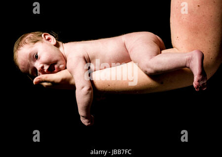 Ein kleines neugeborenes Baby wird auf der mano der Mutter getragen und zufrieden schaut aus, freigestellt vor schwarzem Hintergrund. Foto Stock