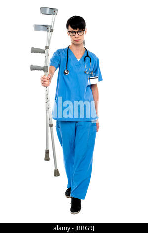 Triste medico tenendo su stampelle in mano e camminare verso la telecamera. Foto Stock