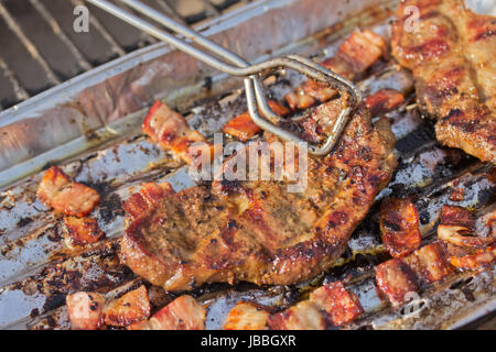 Bistecca alla griglia e la pancetta su un vassoio di alluminio, che impedisce il gocciolamento il grasso nel fuoco. Foto Stock