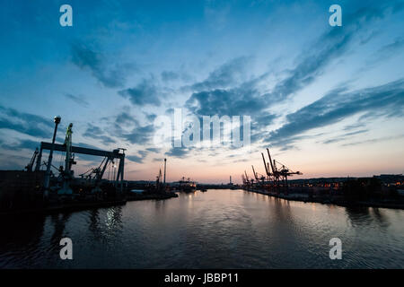 Gru di banchina nel terminale di carico con forme visibili di contenitori contro il Cielo di tramonto sfondo, vivible Porto entrata e porto. Foto Stock