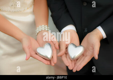 L uomo e la donna, elegantemente vestito, abito nuziale, tenendo simbolico cuori di argento nelle loro mani, softfocus, visibile irriconoscibile frammenti di corpo, modello di rilascio non richiesto. Foto Stock