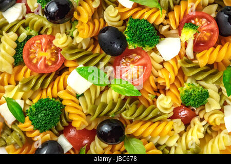 Un primo piano di una insalata di pasta. Rotini di vari colori, verde e fresco di foglie di basilico, olive nere, la mozzarella a fette, broccoli, e ciliegia per Foto Stock