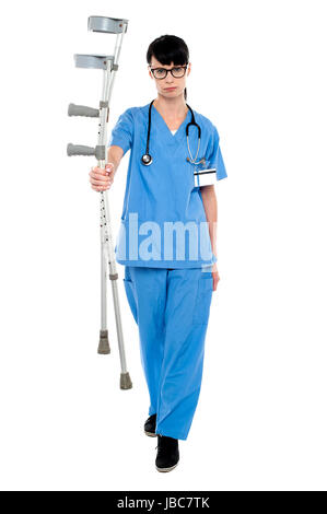 Triste medico tenendo su stampelle in mano e camminare verso la telecamera. Foto Stock