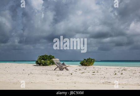 Tabella di rotte e di legno sede Sun, su di una spiaggia deserta alle Maldive. Cielo tempestoso overhead con il grigio monsone di nuvole. Foto Stock