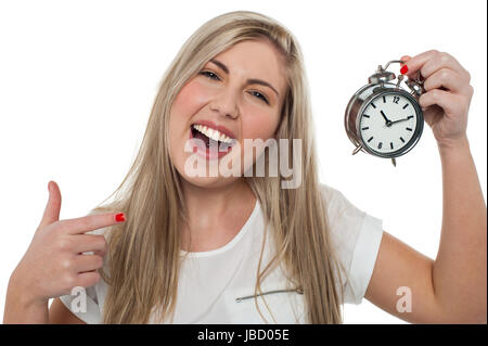 Espressione di un Excited donna ascolto di campanelli di allarme, puntando verso l'orologio. Foto Stock