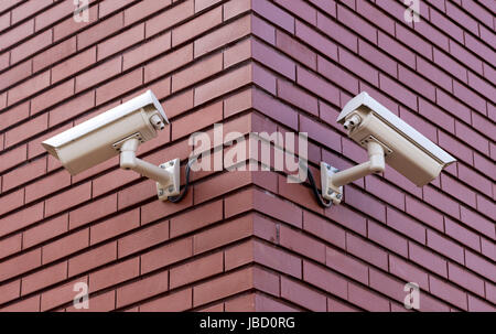 Due telecamere di sicurezza sul muro di mattoni che si affaccia su lati opposti Foto Stock