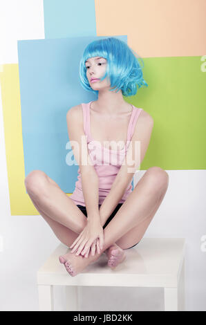 Patchwork. Funky Girl in azzurro parrucca seduto in Studio sulla sedia bianca Foto Stock