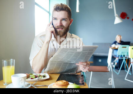 Giovane uomo con i giornali per leggere le notizie e chiamata di un collega Foto Stock