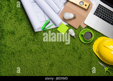 Il luogo di lavoro con casco, blueprint, laptop e blocco note su sfondo di erba. Vista da sopra con lo spazio di copia Foto Stock