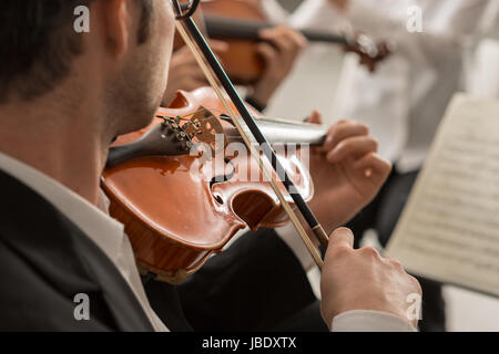 Il violinista di eseguire sul palco con musica classica Symphony Orchestra e con le mani vicino, il fuoco selettivo irriconoscibile persone Foto Stock