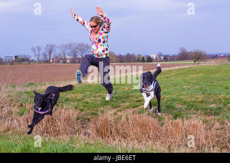 Junge Frau springt mit Hunden über einen Graben Foto Stock