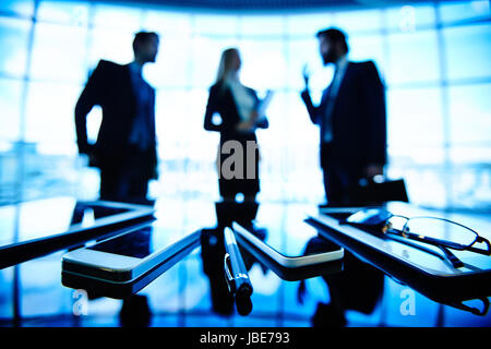 Immagine di occhiali, penna, i telefoni cellulari e i touchpad presso il luogo di lavoro con imprenditori negoziando sullo sfondo Foto Stock