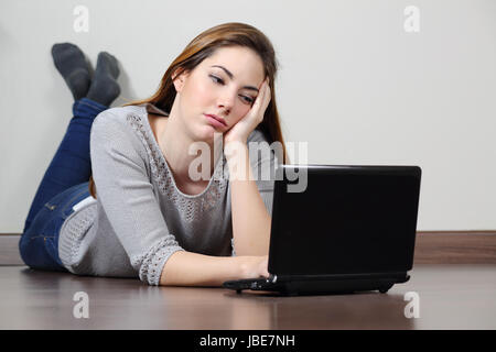 Annoiati ragazza adolescente browsing social media in un notebook sdraiato sul pavimento a casa Foto Stock