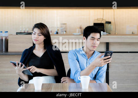 Asian giovane guardando il loro telefono mobile mentre su una data nel cafe. Giovani asiatici giovane seduto e utilizzando il loro smartphone ignorando ogni altro. Foto Stock