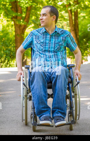 Giovane uomo in sedia a rotelle godendo di aria fresca nel parco della città Foto Stock
