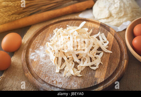 Freschi di pasta fatta in casa con ingredienti per la pasta nel buio di un tavolo di legno vicino fino Foto Stock