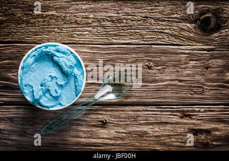 Cool blue rinfrescante gelato italiano in una vasca da asporto con un cucchiaio di plastica per un trattamento di benvenuto in una calda giornata estiva è servita su un vecchio tavolo di legno con copyspace, vista da sopra Foto Stock