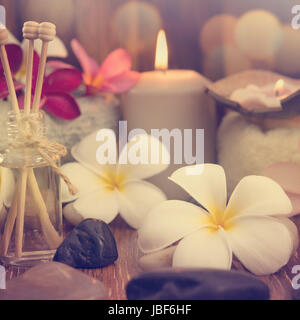 Wellness e spa concept con candele, fiore di frangipani, legno di sandalo e rattan bastoni su lettino da massaggio in vintage stile retrò. Foto Stock