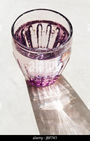 Viola sfaccettata in vetro con acqua sorgiva illuminata dalla luce del sole Foto Stock