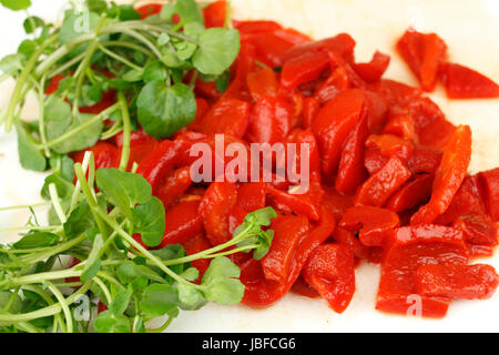 Nutriente e gustosa foglie di crescione con arrosti di peperone rosso pezzi su un bianco tagliere closeup. Foto Stock