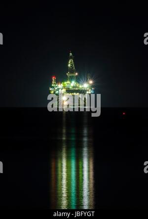 Una vista notturna dell'olio piattaforma di trivellazione illuminato sulla costa di Limassol, Cipro. La piattaforma petrolifera è fluttuante nel mare Mediterraneo ed è pronta per la foratura per il gas naturale valutazione. Foto Stock