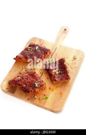 Porzioni di spicy BBQ Ribs condito con condimenti aromatici ed erbe fresche su un tagliere di legno isolato su bianco Foto Stock