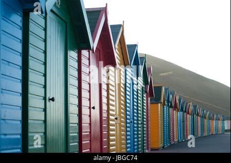 Riga di colorate cabine in legno che si affaccia su sabbie di Whitby nel North Yorkshire cercando lungo la facciata anteriore della linea sfuggente di capanne Foto Stock