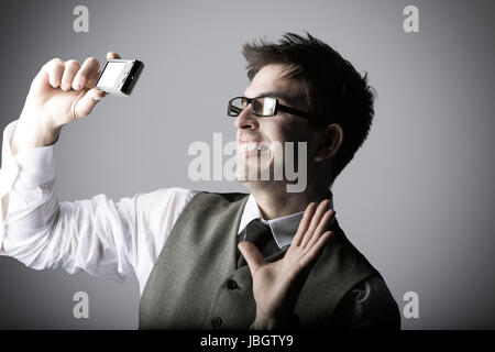 Ridendo giovane fa un selfie con una fotocamera compatta contro uno sfondo grigio Foto Stock