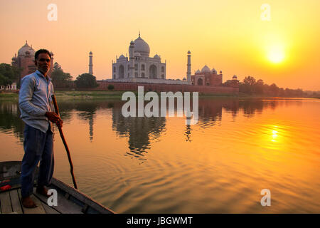 Locali sterzo uomo barca sul fiume Yamuna al tramonto nella parte anteriore del Taj Mahal, Agra, India. Esso fu costruito nel 1632 dall'imperatore Shah Jahan come memoriale per la sua Foto Stock