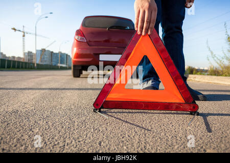 Closeup foto di un uomo mettendo triangolo segno di avvertimento sulla strada Foto Stock