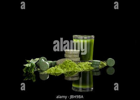 Spirulina, clorella, wheatgrass e lame barleygrass, pillole, massa in polvere e il succo verde in vetro isolato su sfondo nero. Medicina alternativa. Foto Stock