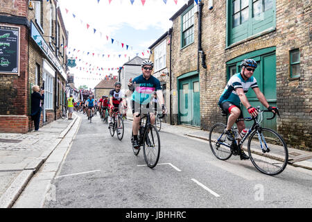 I ciclisti di avviare il Le Tour de ciclo Sandwich Sportif. Molti ciclisti equitazione biciclette verso spettatore attraverso le strette strade della città. Bunting appeso sopra la testa. Foto Stock