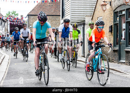 I ciclisti di avviare il Le Tour de ciclo Sandwich Sportif. Molti ciclisti equitazione biciclette verso spettatore attraverso le strette strade della città. Bunting appeso sopra la testa. Foto Stock