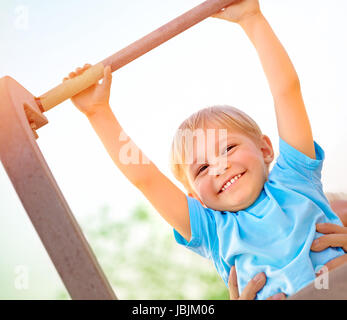 Ragazzino con padri aiutare a recuperare il ritardo accumulato sulla barra orizzontale, attiva l'infanzia, carino piccolo acrobat, allenamento sul cortile, summer camp concept Foto Stock