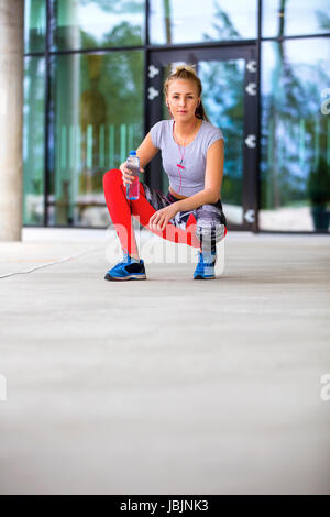 Donna sportivo tenendo la bottiglia di acqua mentre accovacciato sul sentiero Foto Stock