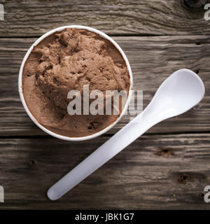 Vicino la vista da sopra di un vasetto di crema di cioccolato Italiano o moca gelato servito con un monouso cucchiaio in plastica su un vecchio textured tavolo in legno, formato quadrato Foto Stock