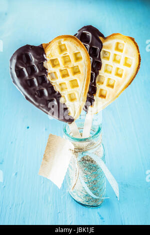 Due romantici a forma di cuore cialde dorato immersi nel cioccolato simbolica dell amore su un bastone in un vasetto di vetro con tag regalo per una fidanzata su un occasione speciale o di celebrazione Foto Stock