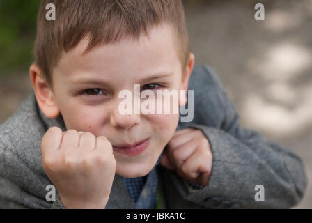 Piccolo Ragazzo sorridente minaccia con i pugni tenendo il pugilato rack Foto Stock