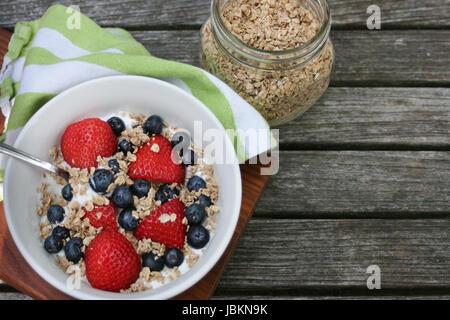 Sana colazione ciotola. Granola in bianco ciotola con lo yogurt greco e bacche su sfondo di legno Foto Stock