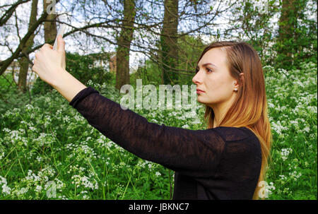 Una giovane donna prendendo un selfie in un campo di fiori selvatici Foto Stock