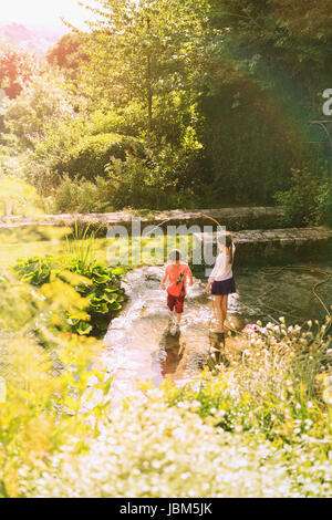 Un ragazzo e una ragazza del fratello e sorella giocando con il tubo flessibile nel soleggiato giardino estivo Foto Stock