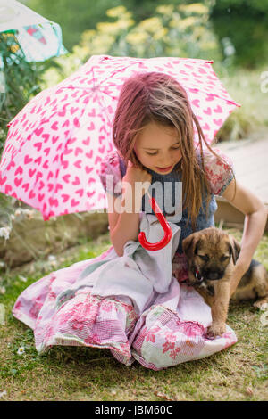 Ragazza con cucciolo di cane tenendo cuore forma di ombrello in erba Foto Stock