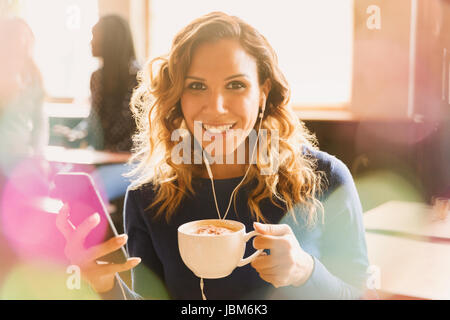 Ritratto di donna sorridente con le cuffie per ascoltare musica sul lettore mp3 e di bere il cappuccino in cafe Foto Stock