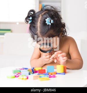 Una piccola ragazza indiana ingrandire giocattoli attraverso una lente di ingrandimento, vivere lifestyle a casa. Foto Stock