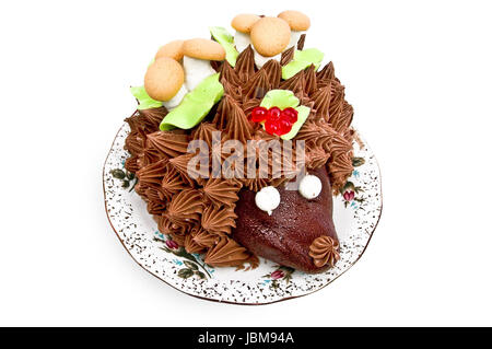 Torta a forma di riccio, ornata con foglie verdi con crema di funghi da biscotto e meringa, bacche, jelly su una piastra isolata su uno sfondo bianco Foto Stock
