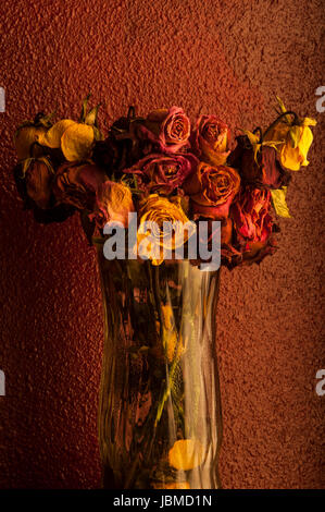 Rose multicolori avvizzimento in vaso di vetro con una calda luce della finestra Foto Stock