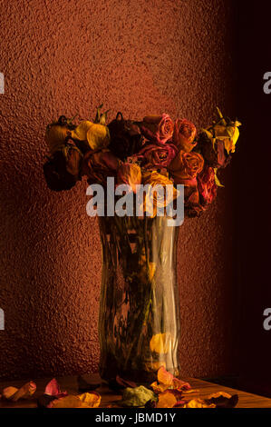 Rose multicolori avvizzimento in vaso di vetro con una calda luce della finestra Foto Stock